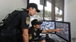 Two security guards monitoring multiple CCTV screens in a control room